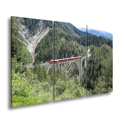 Leinwandbild Ein roter Zug schwebt über ein grünes Meer aus Tannen. - deyoli