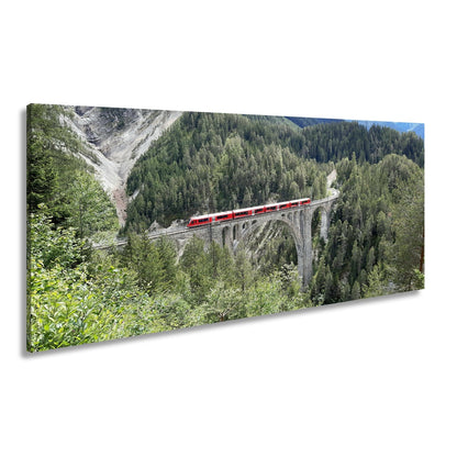 Leinwandbild Ein roter Zug schwebt über ein grünes Meer aus Tannen. - deyoli
